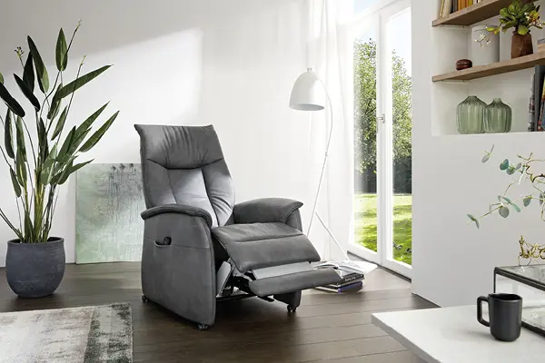 Grauer Relaxsessel mit verstellbarer Fußstütze in einem hellen Wohnzimmer mit Parkettboden und großen Fenstern – bequemer Fernsehsessel, moderner Ruhesessel, Relaxfunktion, gemütliche Sitzgelegenheit für stilvolle Wohnräume.